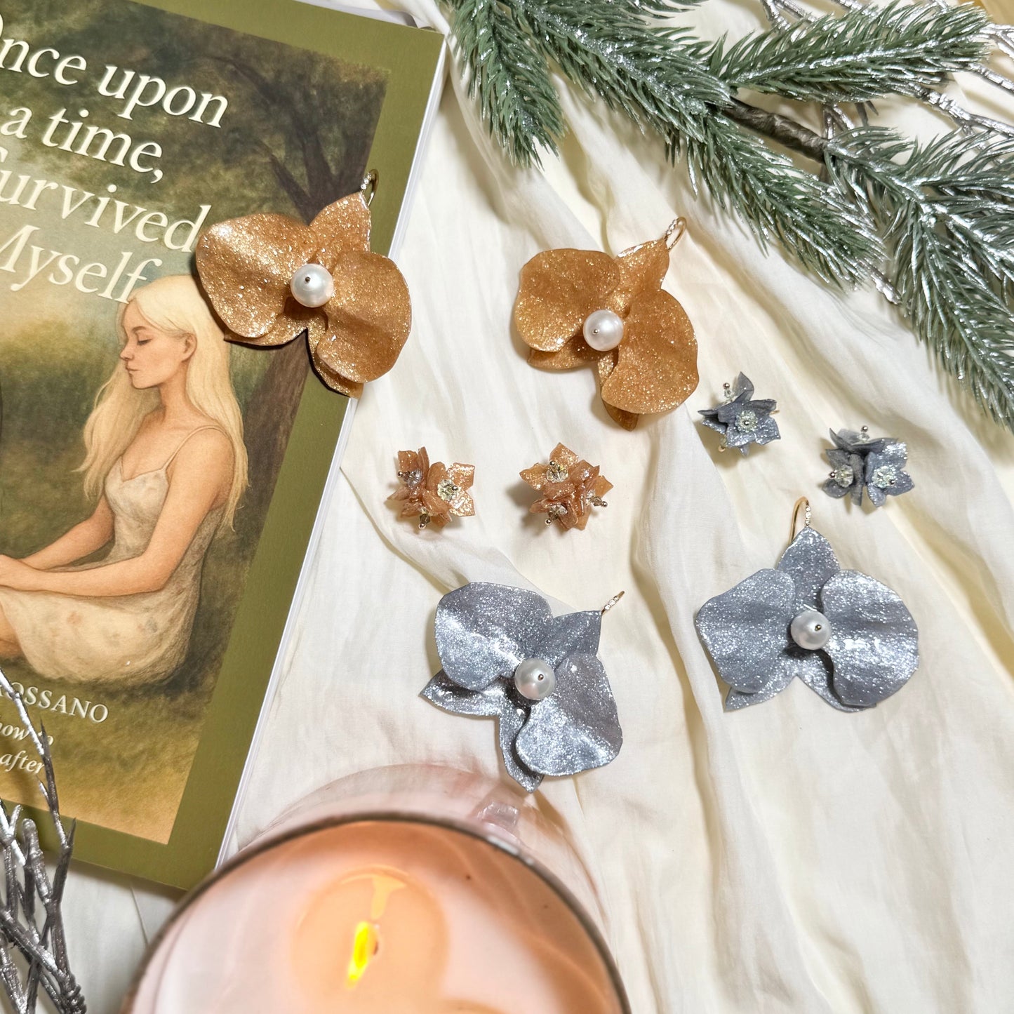 Earrings on a textured surface with a candle and decorative card.